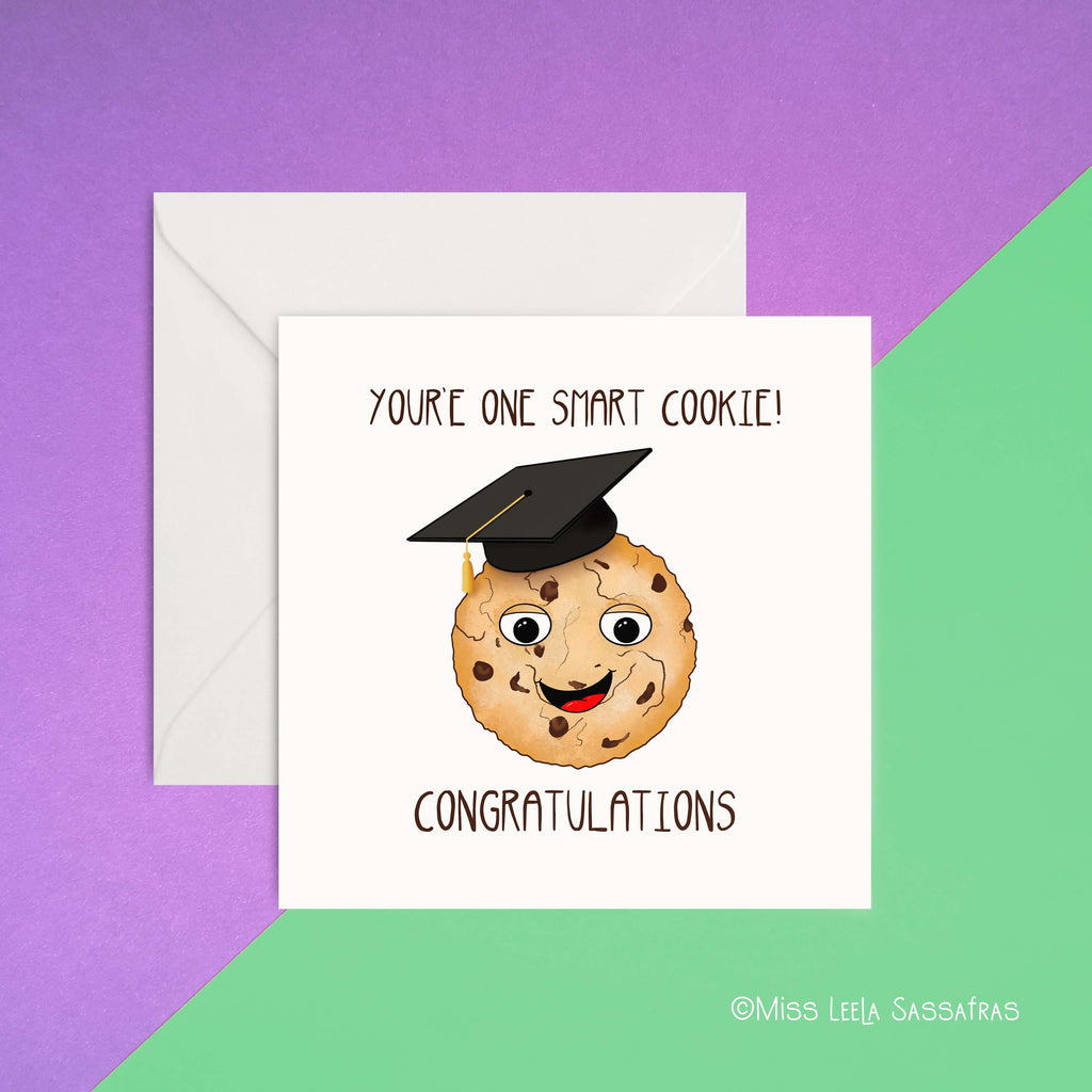 A card with you’re one smart cookie congratulations written on it .Illustration of a cookie with a smiling face and a graduation  hat on it. 